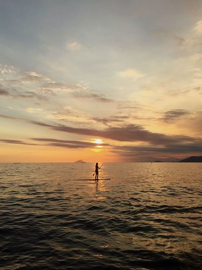 Silhouette person standing in sea against sky during sunset