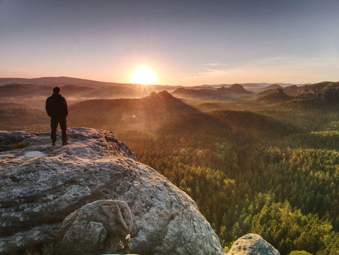 Man on the rock empire with hands in trousers pocket watch over the misty morning valley to sun