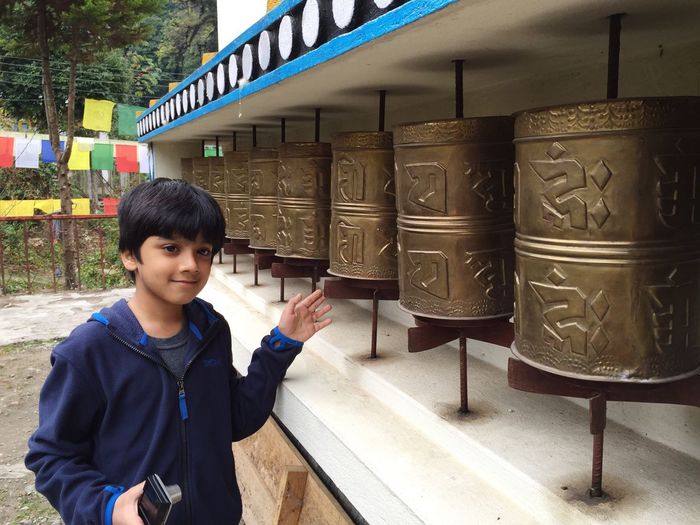 Boy looking away while standing by prayer wheels