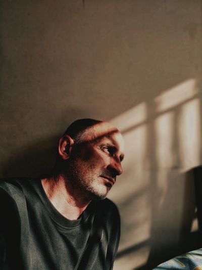 Mature man looking away while sitting against wall