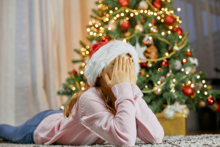 A cute girl lies by the christmas tree and dreams. dreams come true. children waiting new year
