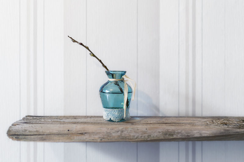 Turquoise glass vase with a catkin branch stands on old wood in front of bright wallpaper