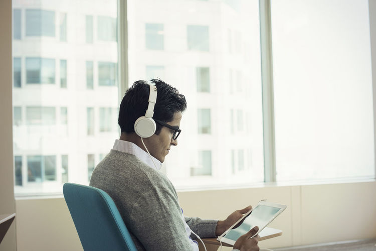 Businessman sitting in chair, wearing headphones, using digital tablet