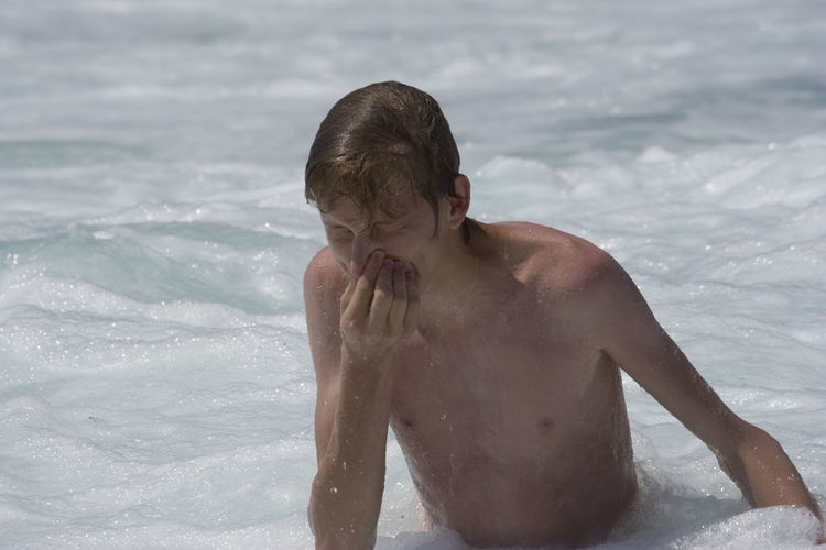 High angle view of shirtless man holding his nose with eyes closed in sea at beach