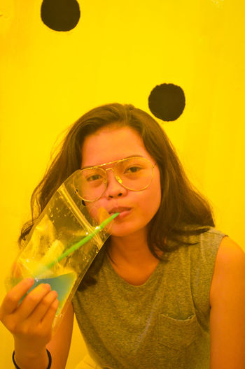 Close-up portrait of girl drinking against yellow wall