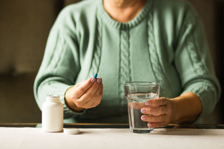 Woman's hands holds a blue capsule and glass of water. ready to take medicines. health care concept.