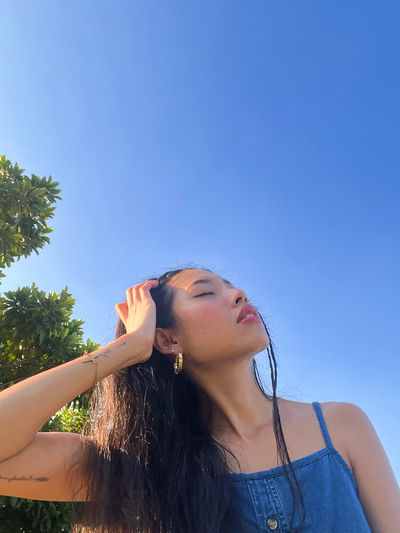 Low angle view of young woman drinking water against clear blue sky