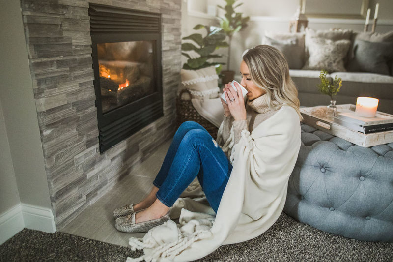 Woman drinking coffee while sitting by fireplace at home