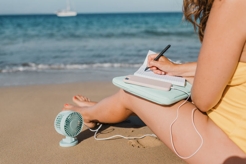 Young woman reading book while sitting at beach