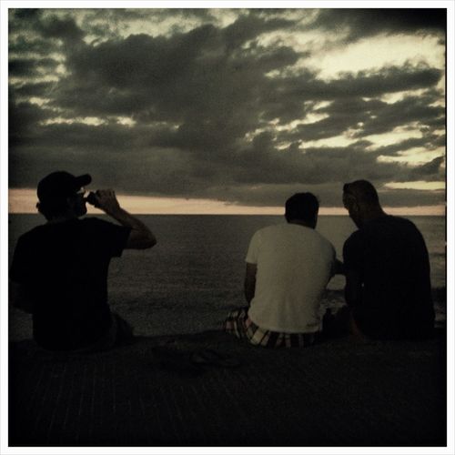 People sitting on beach against cloudy sky