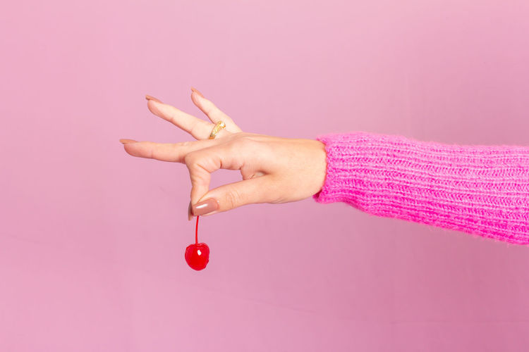 Cropped hand of woman holding heart shape against pink background