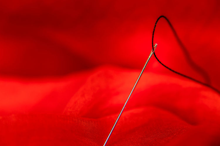 Close-up of thread in needle against red fabric