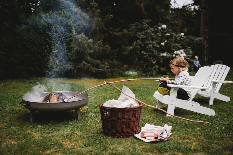White child holding stick sitting on chair making smores in bonfire