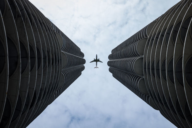 Low angle view of modern buildings against sky with airplane 