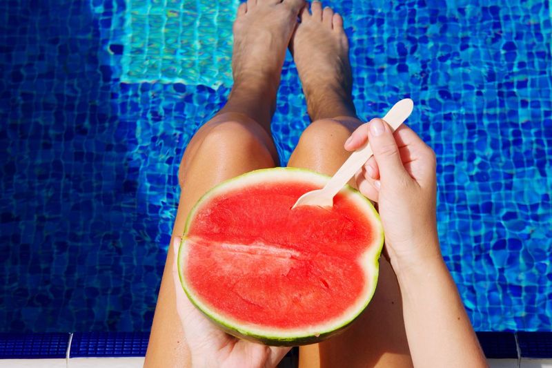 Midsection of woman holding water melon over swimming pool