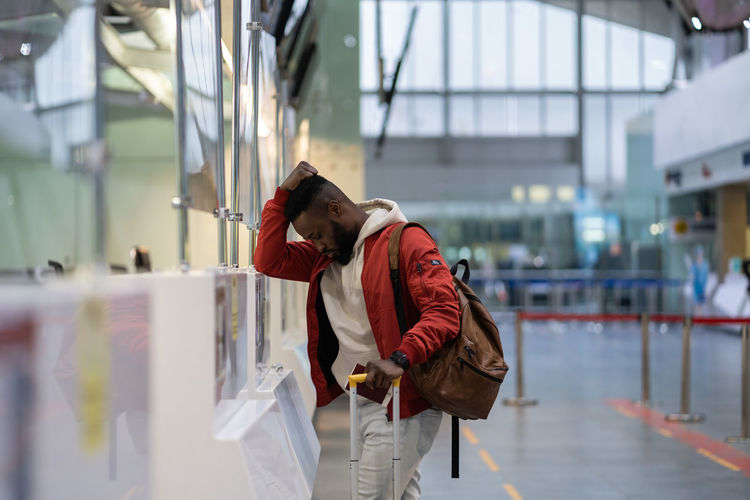 Frustrated sad young african man passenger having problems with check-in for flight