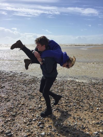 Man carrying girlfriend while walking on shore at beach