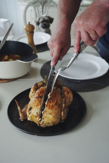 Cropped hand of woman cutting roasted chicken in plate