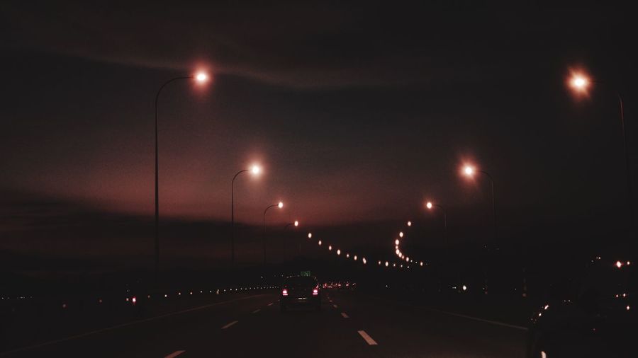 Cars on illuminated road against sky at night