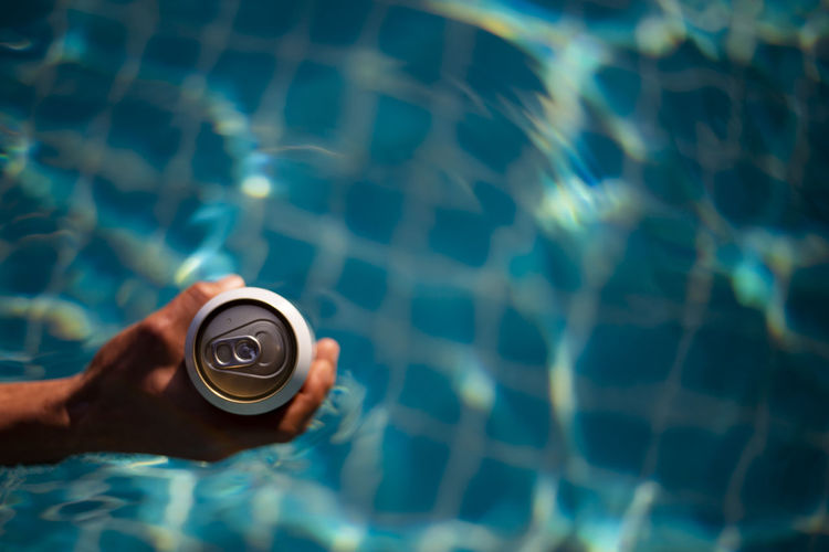 Selective focus white beer can in hand. man is soaking in the pool with an open beer can relax