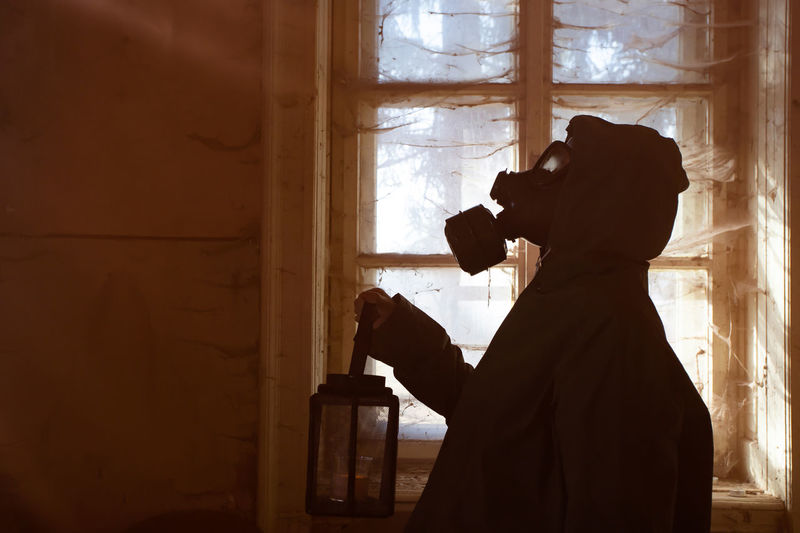Woman holding oil lamp wearing gas mask standing amidst smoke