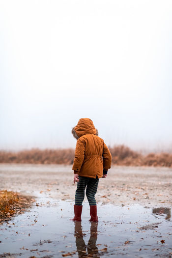 Small boy standing in a mud puddle on a gravel road in the fog