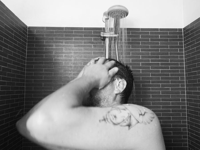 Shirtless man taking bath from shower