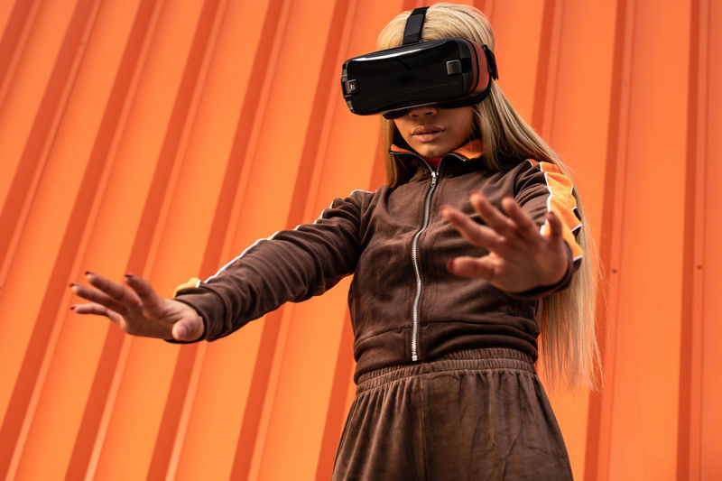 Pretty african american woman using virtual reality glasses on an orange background