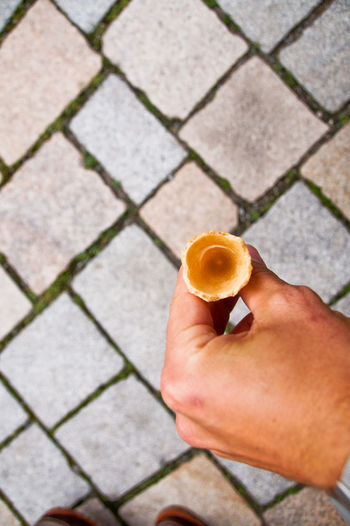 Cropped image of hand holding ice cream cone on paved footpath