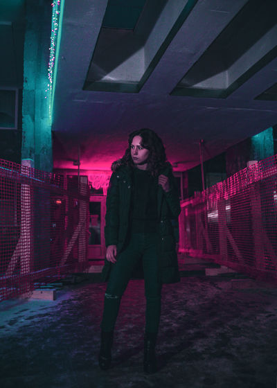 Full length portrait of young woman standing against illuminated building