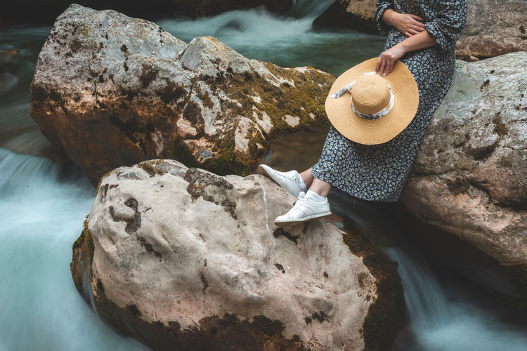 Woman relaxing on the river rocks with hat in summer