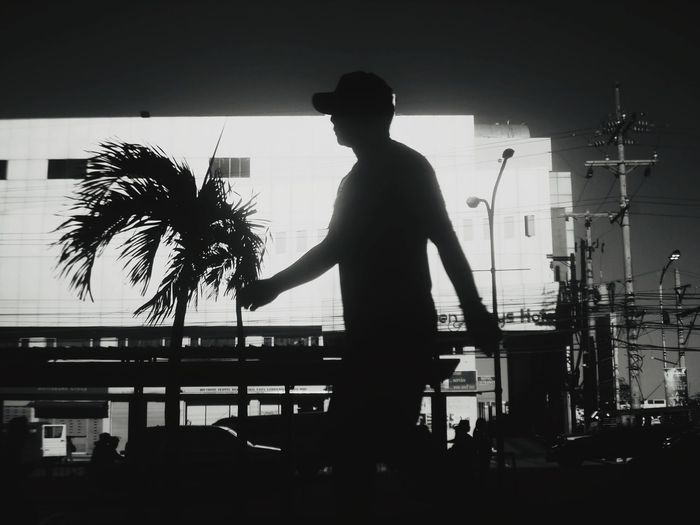 Silhouette man standing by palm trees against sky in city