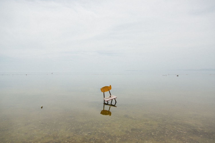 Abandoned chair at sea against sky