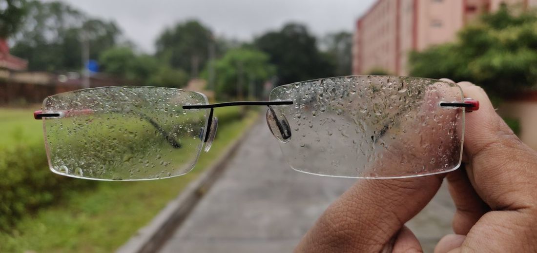 Cropped hand holding wet eyeglasses during rainy season