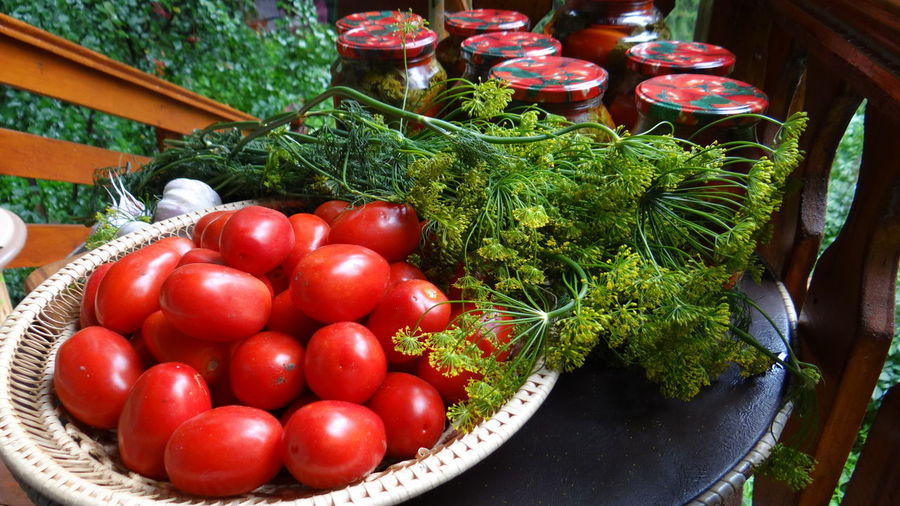 High angle view of tomatoes in bowl by jars and herbs on table