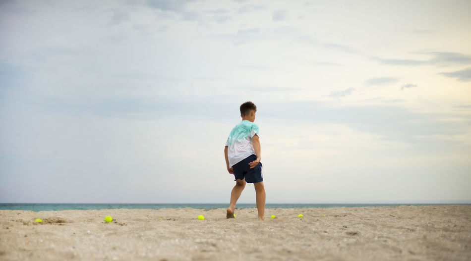 Boy teenager exercising on the sandy beach. physical training. tennis balls.