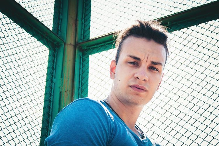 Low angle portrait of young man standing by chainlink fence