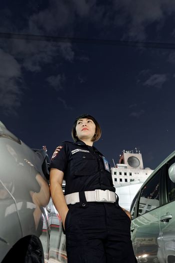Low angle view of female police officer standing by cars against sky