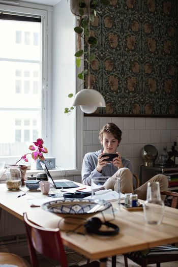 Teenage boy using mobile phone while studying at home