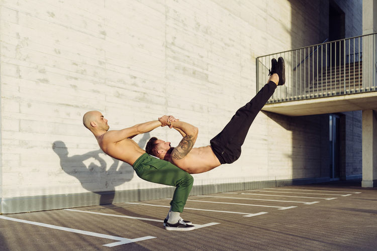 Young athletic shirtless men doing an urban workout outdoors practicing balance exercises