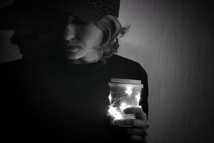 Close-up of woman holding illuminated light bulb against wall