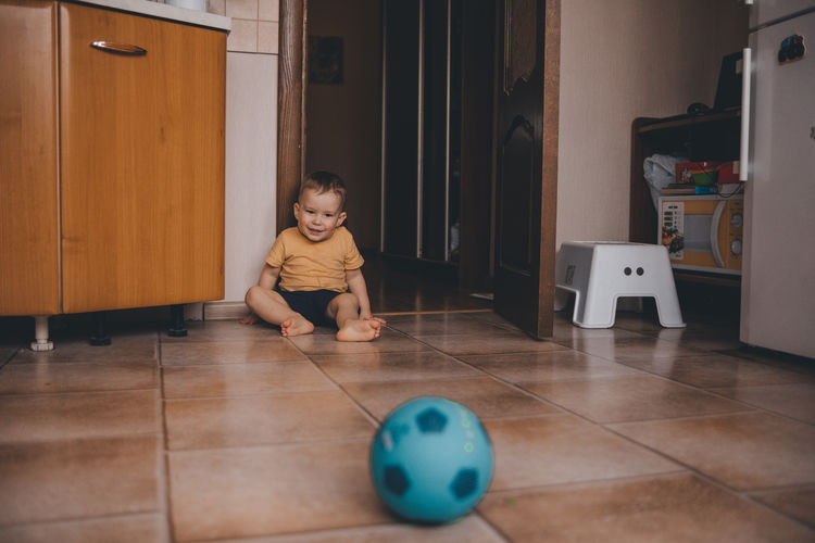 Child sits on the floor at the home and playing in blue ball