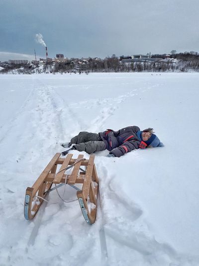 Portrait of carefree boy lying on snow by wooden sled during winter