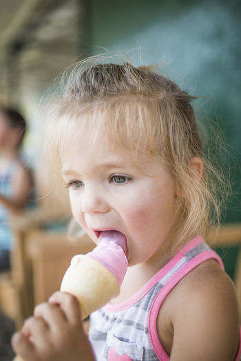 Young cute girl happily licking pink ice cream on summer day.
