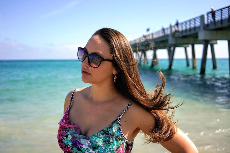 Portrait of young woman wearing sunglasses standing against sea