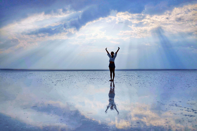 Woman raises arms towards beautiful sky with reflection