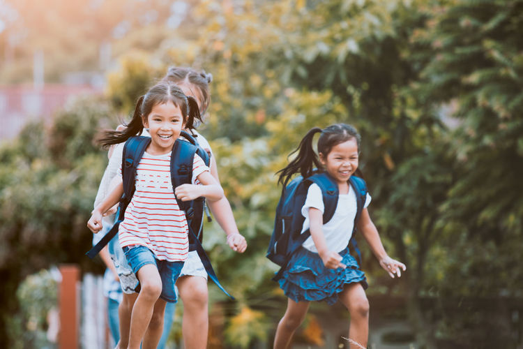 Happy friends running with backpacks against plants