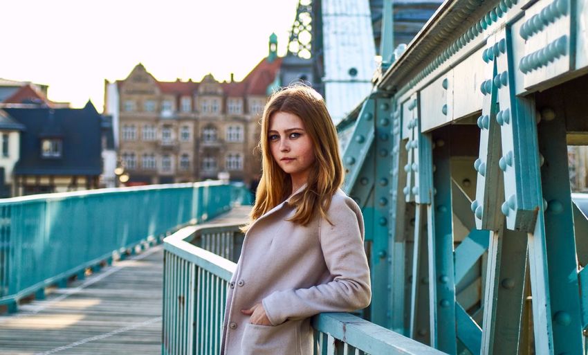 Portrait of beautiful young woman standing by railing on bridge