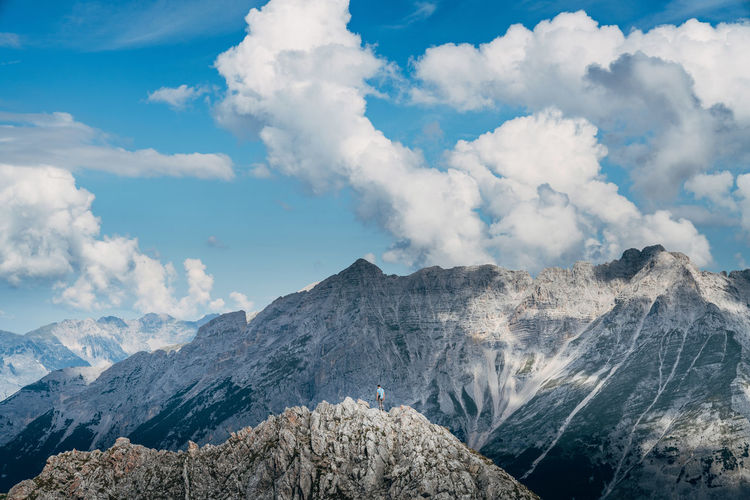 Distant view of hiker on mountain peak against cloudy sky