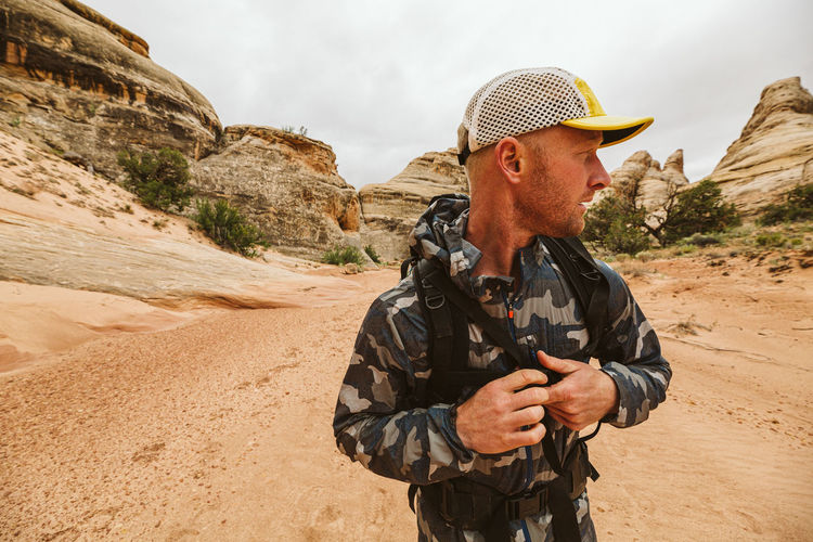Hiker looks left and buckles his chest strap of backpack in desert